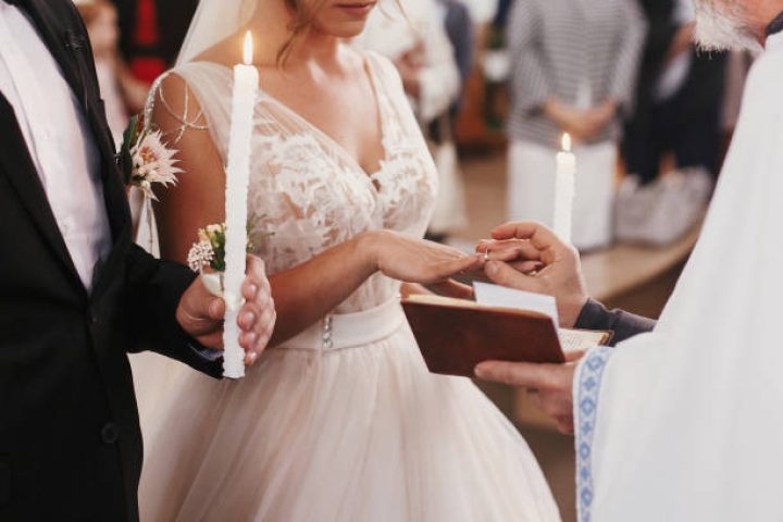 Priest putting on golden wedding ring on bride finger. Wedding matrimony in church. Exchanging wedding rings